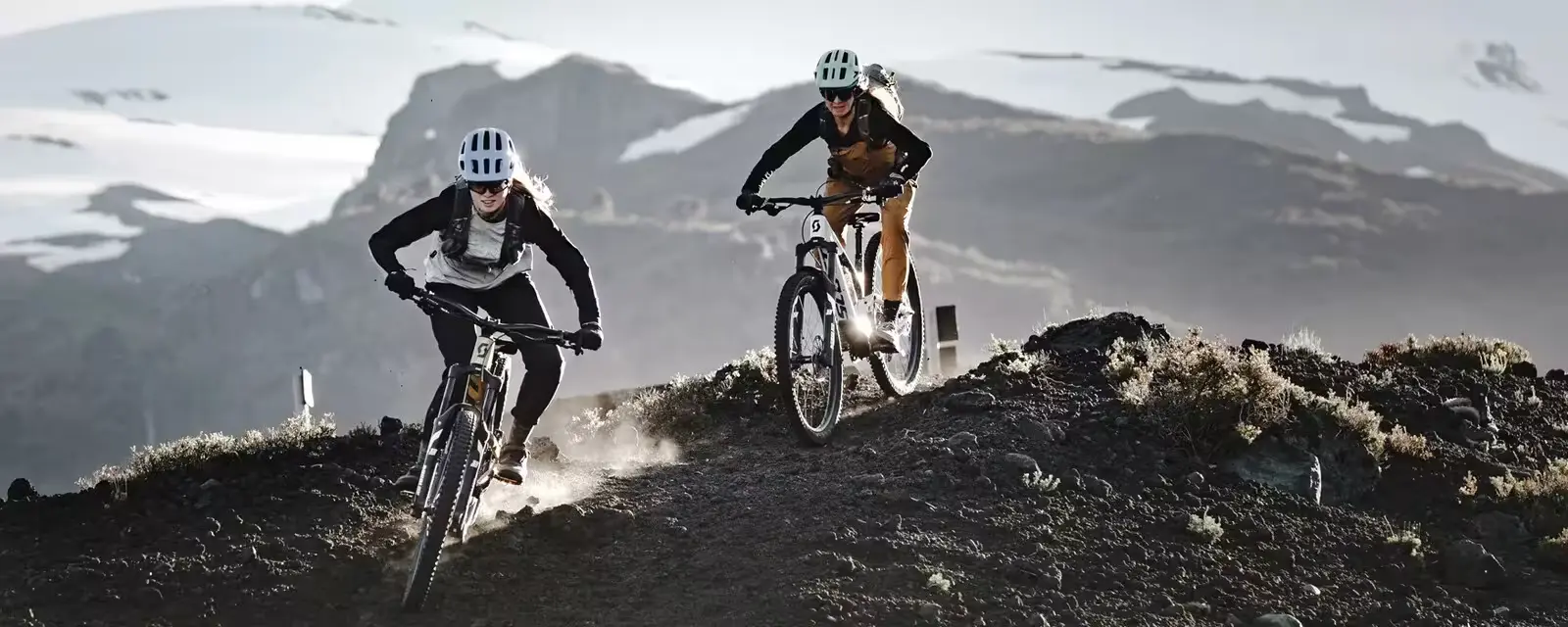 Scott Bike image with two women riding down a trail with mountains in the background.